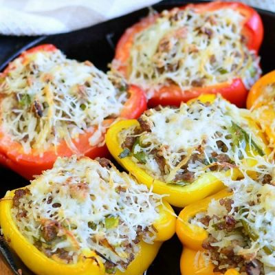 black iron skillet with sausage onion stuffed peppers on a white and tan cloth on wooden table