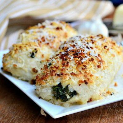 close up view of asiago spinach mushroom chicken tollatini on a white rectangular plate on a wooden table with a white and gold striped cloth in the background to the left