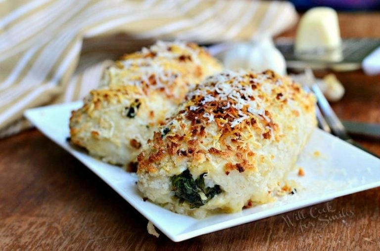 close up view of asiago spinach mushroom chicken tollatini on a white rectangular plate on a wooden table with a white and gold striped cloth in the background to the left