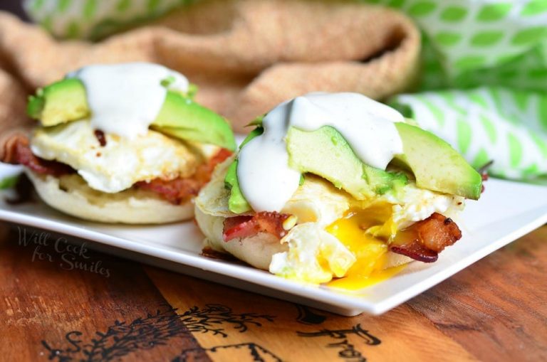 close up view of white rectangular plate with an avocado bacon ranch breakfast on a wooden table with brown cloth topped with a white and green cloth