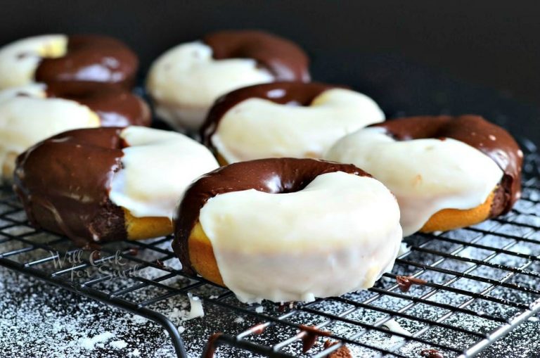 close up view of Black and white glazed donuts on a cooling rack on a black table with powdered sugar on table