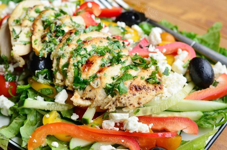 close up view of white rectangular plate with a black rim whit greek chicken salad on a wooden table