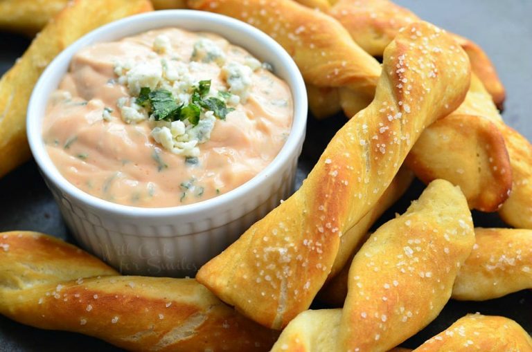 white crock filled with creamy buffalo dipping sauce surounded by homemade soft pretzel twists viewed close up and slight above the twists