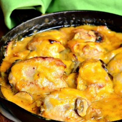 Black skillet with spicy honey mustard chicken on a wooden table with a green cloth in the background.