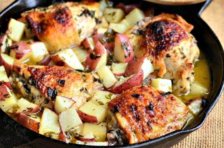 view from above of black skillet with one pot balsamic chicken thighs and potatoes on a tan burlap placemat with a wooden spoon resting on skillet.