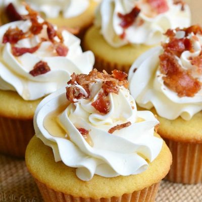 view from the front of 4 maple bacon cupcakes on a burlap cloth on wooden table with a black background