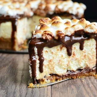 close up view of Smores cheesecake on a wooden table with 1 slice on a cake cutter in front of rest of cake