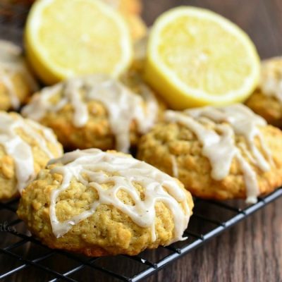 close up view of Glazed cookies on a cooling rack on a wooden table with halved lemons in between cookies