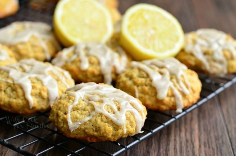 close up view of Glazed cookies on a cooling rack on a wooden table with halved lemons in between cookies