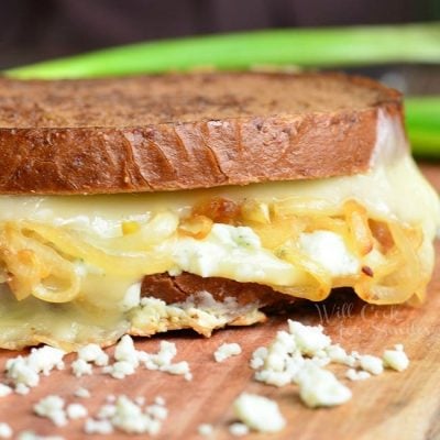 Grilled cheese on a wooden cutting board with blue cheese crumbles in the foreground