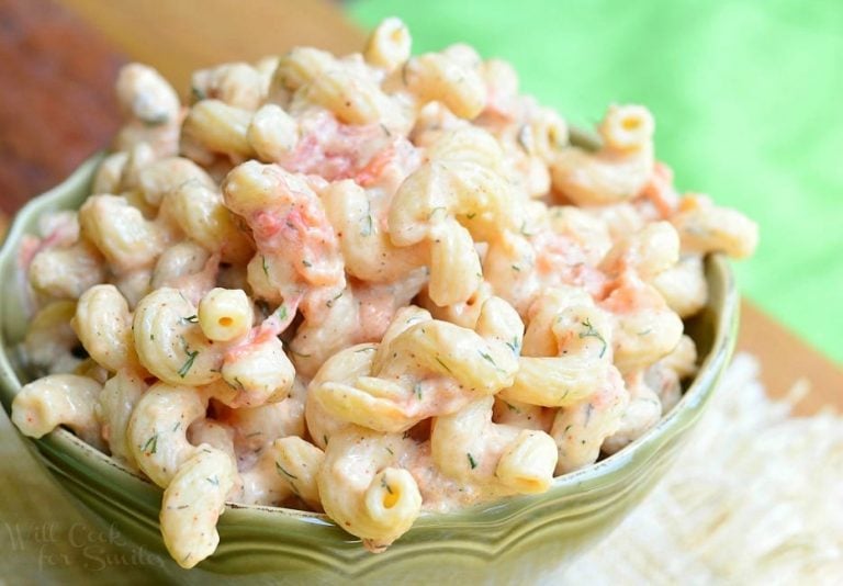 close up view of small green bowl filled with creamy roasted tomato pasta salad on a tan cloth