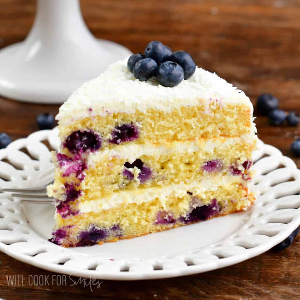 A slice of blueberry cake with cream cheese frosting on a plate.