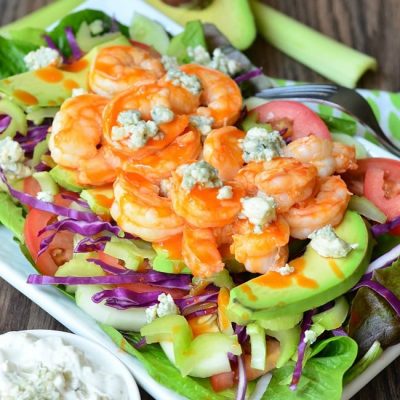 white bowl with homemade blue cheese dressing and a buffalo shrimp salad on a wooden table as seen from above