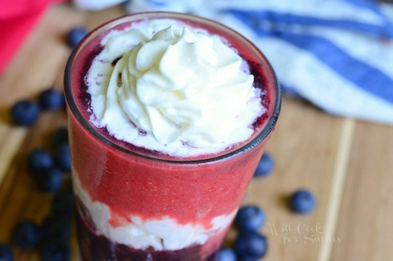 close up view of top of glass with Layered berry daiquiri red white and blue smoothie on a wooden cutting board with blue berries scattered around base of glass