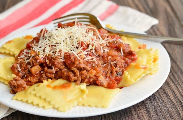 small round white plate with ravioli and meat sauce on a wooden table viewed close up