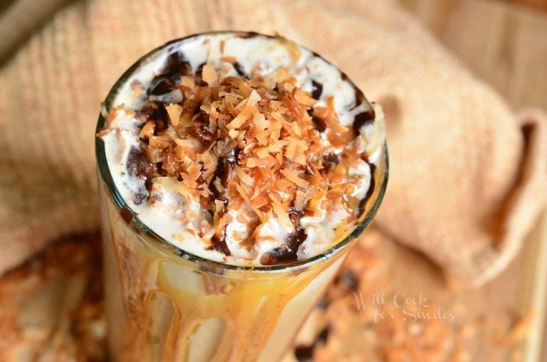 view from above of pint glass filled with samoas frozen coffee on a wooden table with coconut shaving scattered around the bottom of the glass