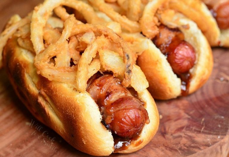 close up view of bbq bacon crsipy onion hot dogs on a wooden table viewed close up