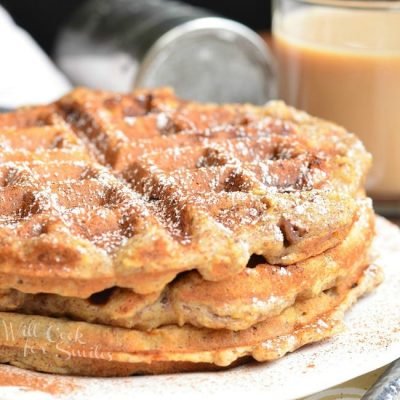 3 stacked cinnamon peach oat waffles on a white plate with a glass of coffe in the background