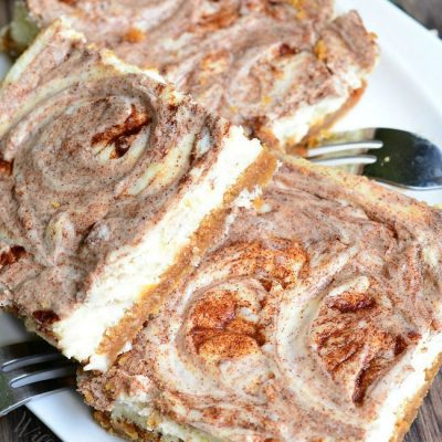 3 cinnamon swirl caramel cheesecake bars on a white plate on wooden table wth 3 forks on plate