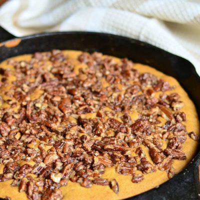 black skillet with a giant pumpkin cookie while sitting on a wooden table with a white cloth in the background