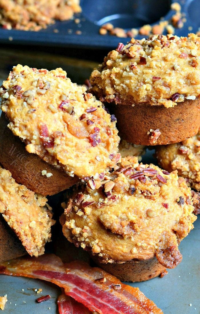 baking pan with maple bacon streusel muffins with strips of bacon below muffins and a muffin pan in the background viewed close up