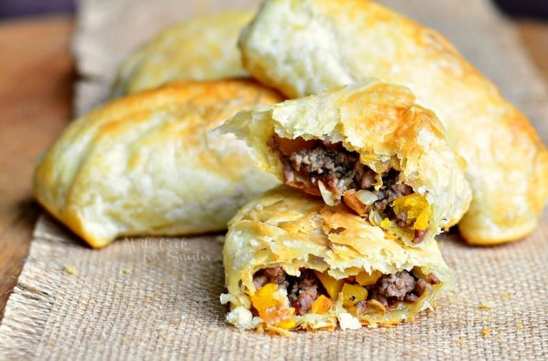 3 pumpkin beef onion hand pies sitting on a tan placemat with the first hand pie broken in half to show inside viewed close up