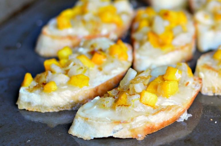 Pumpkin pear brie crostinis on a black surface viewed close up