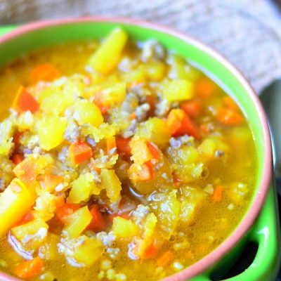 green clay bowl filled with pumpkin sausage soup resting on several cloths