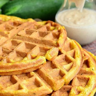 3 zucchini carrot cake waffles stacked on a wooden cutting board