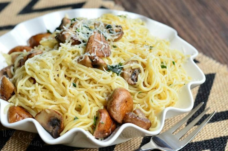 decorative white bowl with truffle pasta and mushrooms on a tan and black placemat on a wooden table as viewed close up