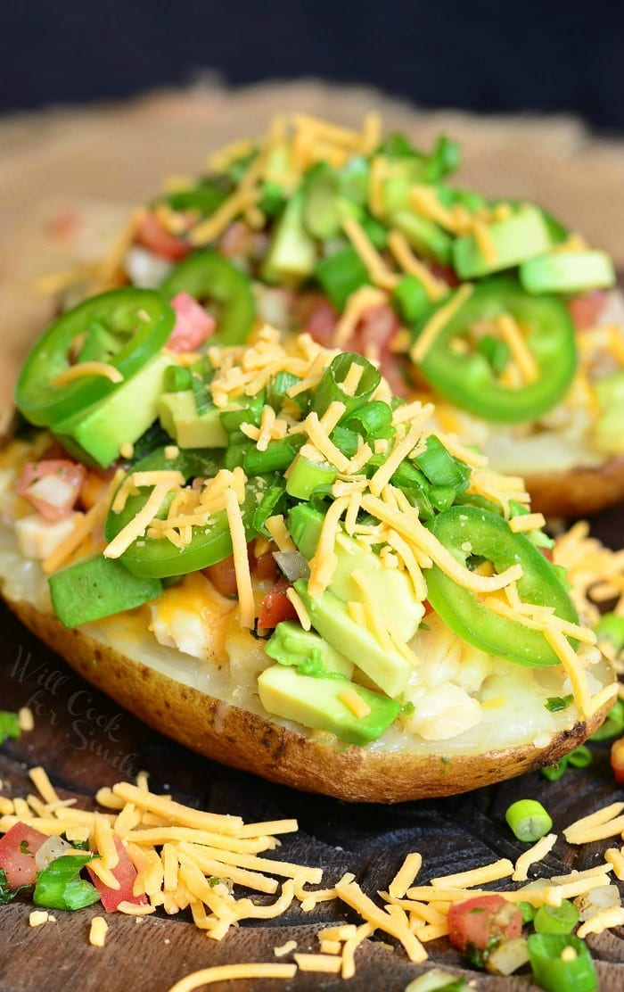 Close up view of fiesta chicken twice baked potatoes on a wooden board topped with chives and sliced jalapenos