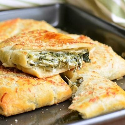 3 spinach artichoke hand pies on a metal baking pan with the top pie broken in half to show contents as viewed close up