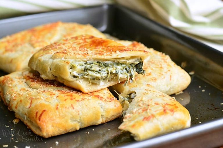 3 spinach artichoke hand pies on a metal baking pan with the top pie broken in half to show contents as viewed close up