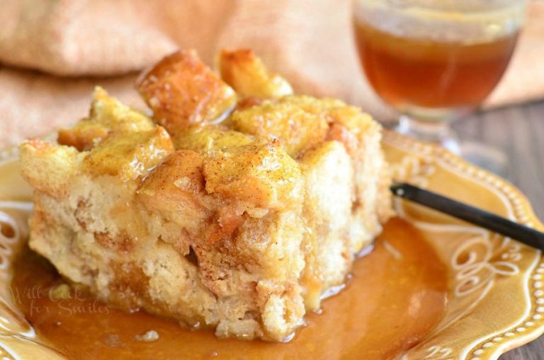 one portion of holiday nog bread pudding with butter brandy sauce on a decorative plate with a brown cloth in the background viewed close up