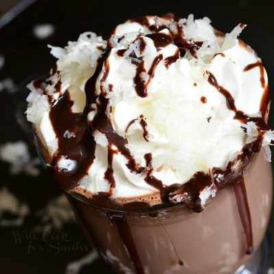 glass coffee mug filled with Mounds Hot Chocolate topped with whipped cream and coconut shavings while additional shavings are scattered around the base of the mug as viewed from above and close up