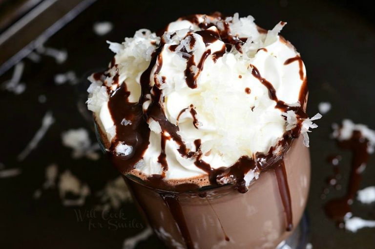 glass coffee mug filled with Mounds Hot Chocolate topped with whipped cream and coconut shavings while additional shavings are scattered around the base of the mug as viewed from above and close up