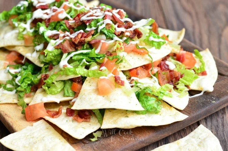 Wooden platter with BLT nachos and homemade baked cool ranch tortilla chips on a wooden table