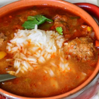 Red clay crock filled with mexican meatballs soup on a white cloth with a spoon in the soup as viewed from above