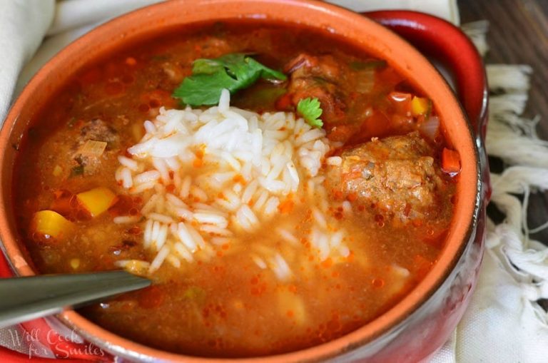 Red clay crock filled with mexican meatballs soup on a white cloth with a spoon in the soup as viewed from above