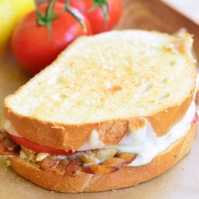 crab tomato and bacon grilled cheese sandwich stacked on a wax paper on a wooden serving tray with 2 vine ripe tomatoes in the background