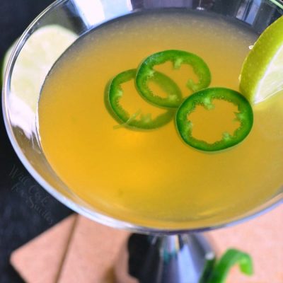 Decorative martini glass filled with Jalapeno Margatini garnished with a slice of lime and a slice of jalapeno leaning up against base of glass as viewed from above