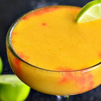 view from above and close up of a sunset margarita garnished with lime while sliced limes rest on a black table by the glass' stem