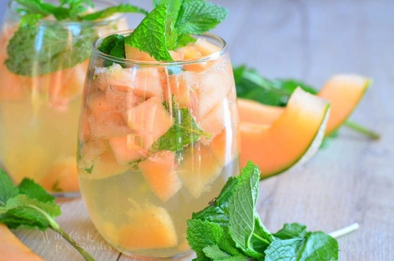 2 glasses filled with melon mint wine spritzer topped with mint leaves on a wooden table as viewed close up