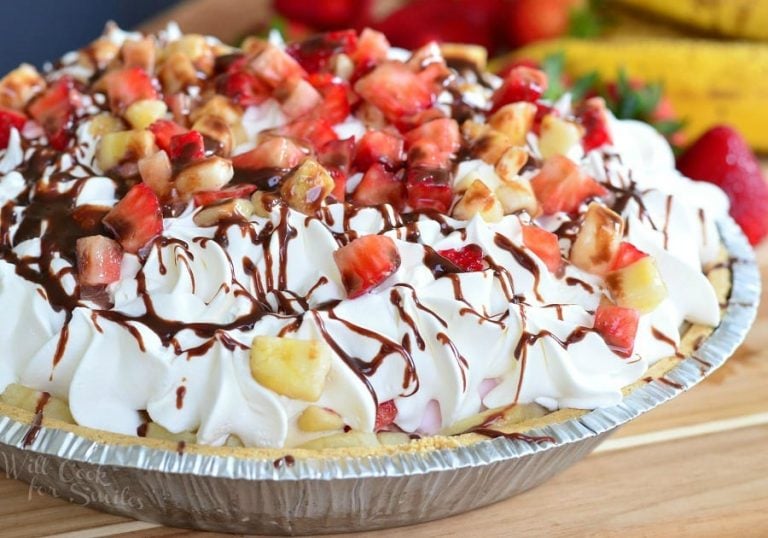 Banana Split Ice Cream Pie on a wooden table with bananas and strawberries in the background as viewed close up