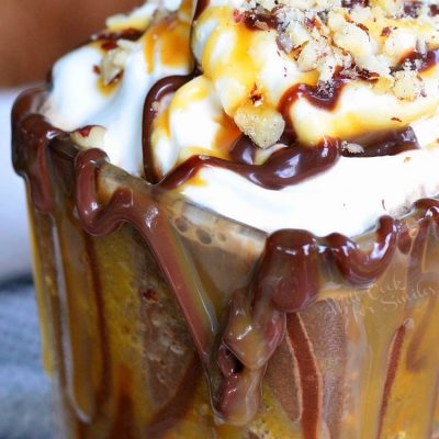 Dessert glass filled with frozen turtle mocha dessert drink topped with turtle crumbs, caramel and fudge as viewed close up and slightly above