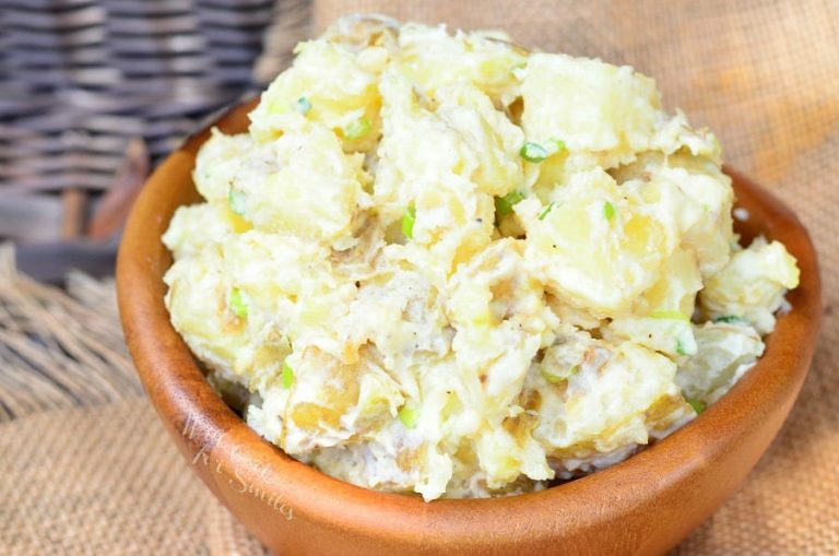 Wooden bowl filled with roasted garlic asiago potato salad on a tan cloth as viewed close up