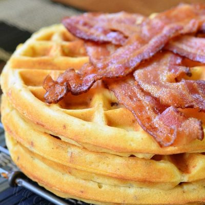 Savory waffles stacked on a metal rack with strips of bacon piled on top of top waffle