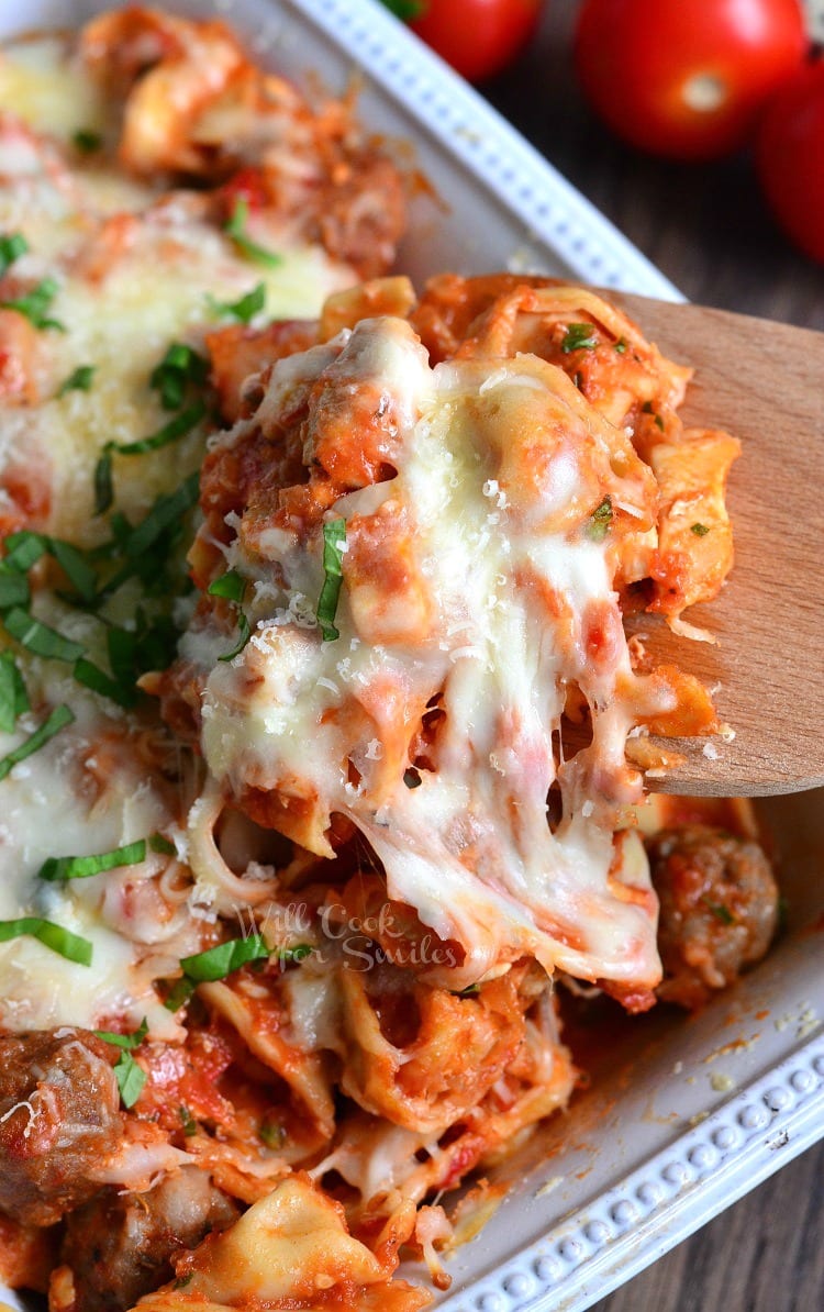 chicken and sausage tortellini casserole in a white decorative baking dish on a wooden table as viewed from above and close up