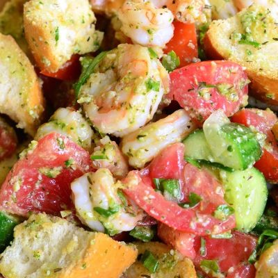 Wooden bowl filled with panzanella salad with shrimp and pesto on a tan placemat as viewed from above and close up