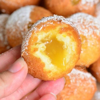 holding Lemon Curd Filled Doughnut with a bite out of it and the rest of the donuts in the background.